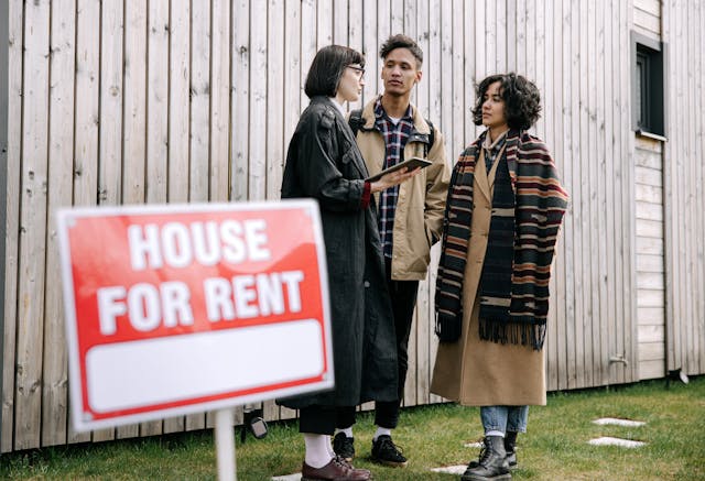 Three people standing outside, behind a house for rent sign